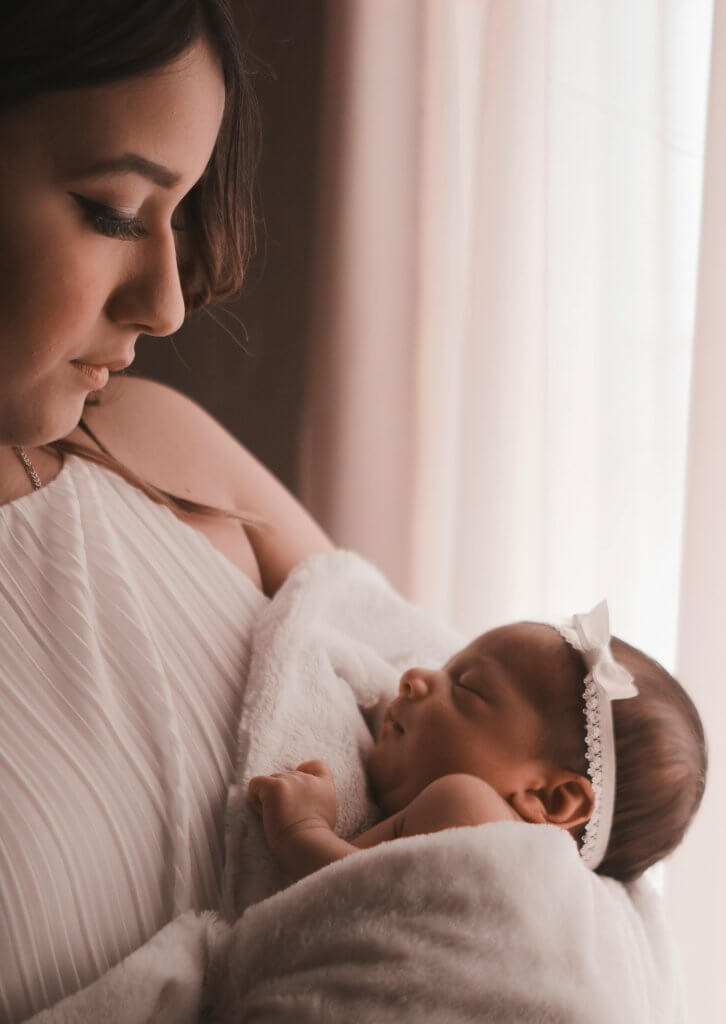 Tender moment of a mother holding her newborn child by a window, capturing love and warmth.