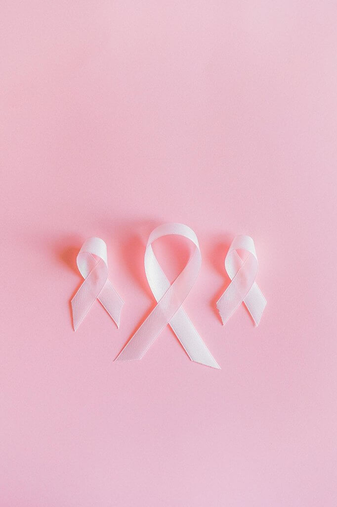 Three pink ribbons symbolize breast cancer awareness on a light pink background.